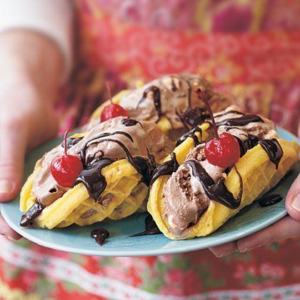 two banana split desserts with chocolate and cherries on top, sitting on a blue plate