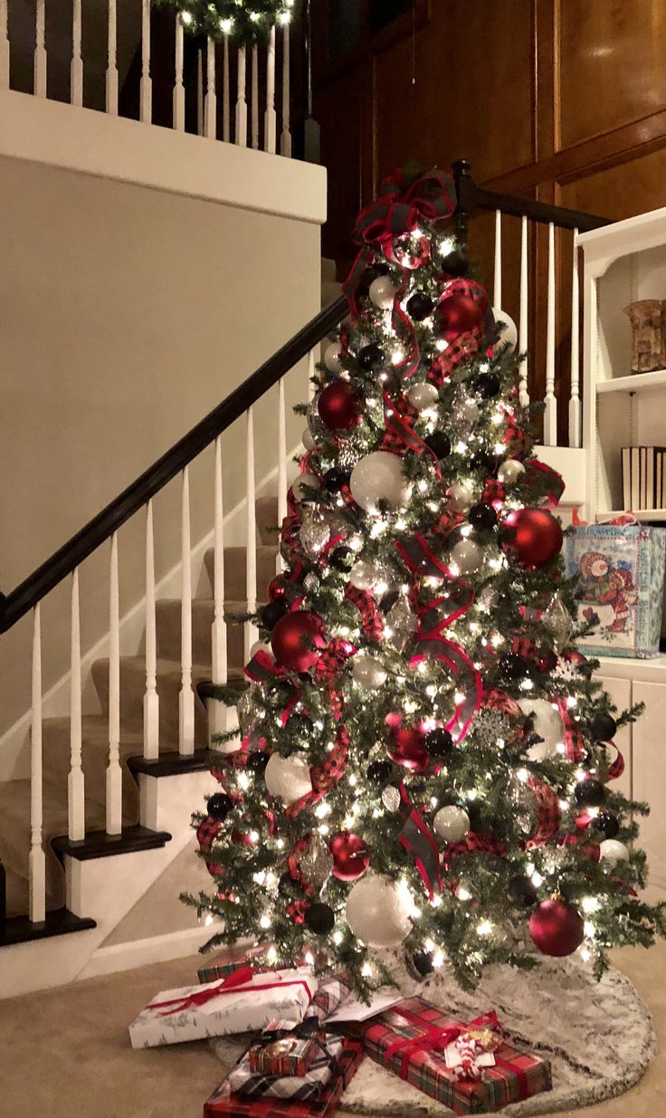 a christmas tree with red and white ornaments on it in front of a stair case