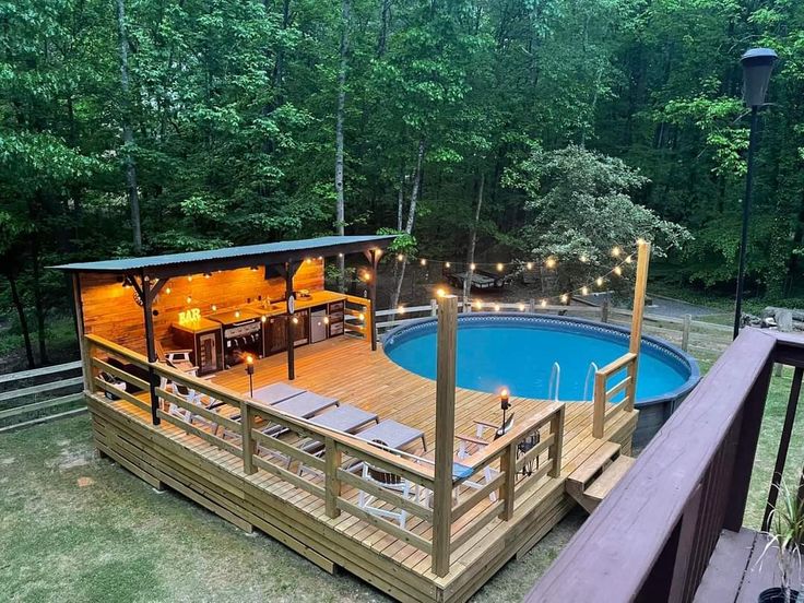 an above ground swimming pool with deck and hot tub surrounded by wooded area at dusk