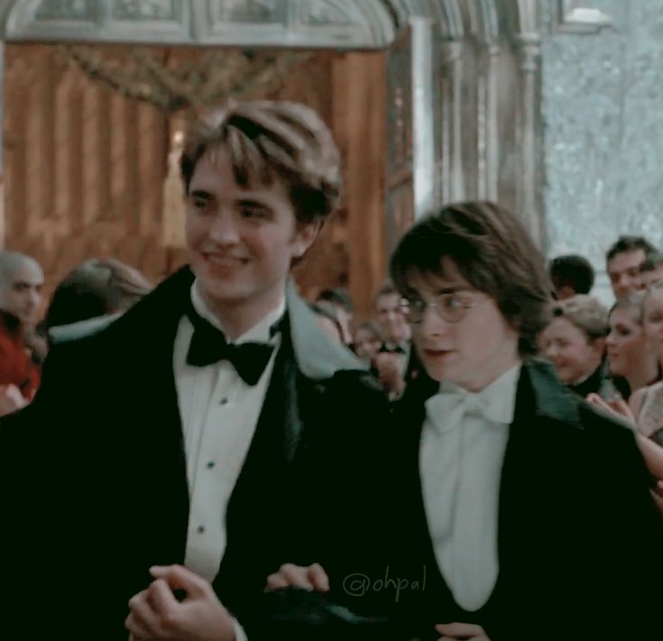 two young men in tuxedos standing next to each other at a formal event