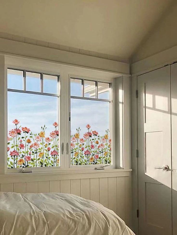 a bed sitting under two windows next to a window sill with flowers on it