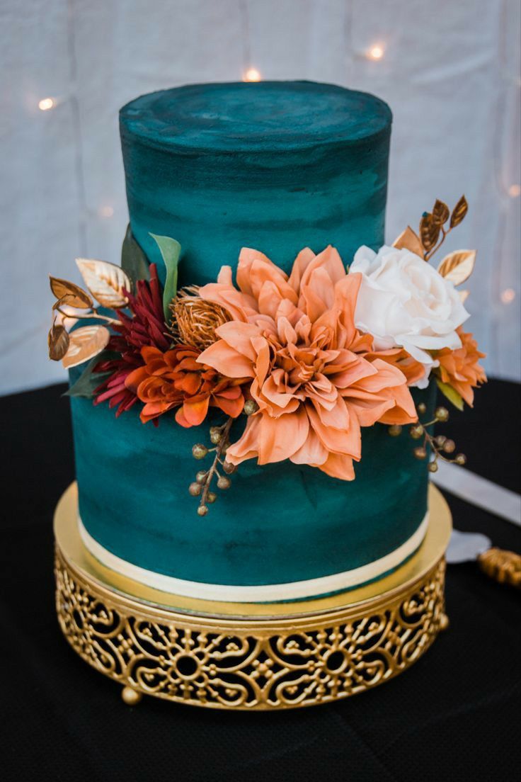 a blue and gold wedding cake with flowers on the top, sitting on a black tablecloth