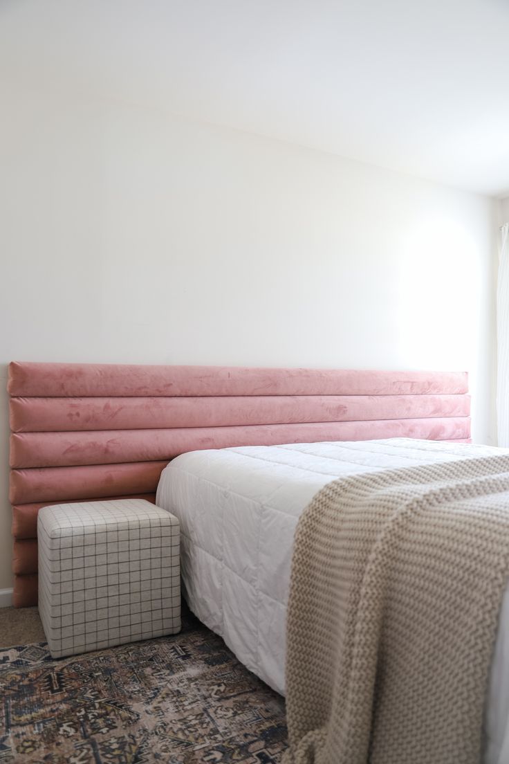 a bed with pink headboard and foot board next to window in white walled room