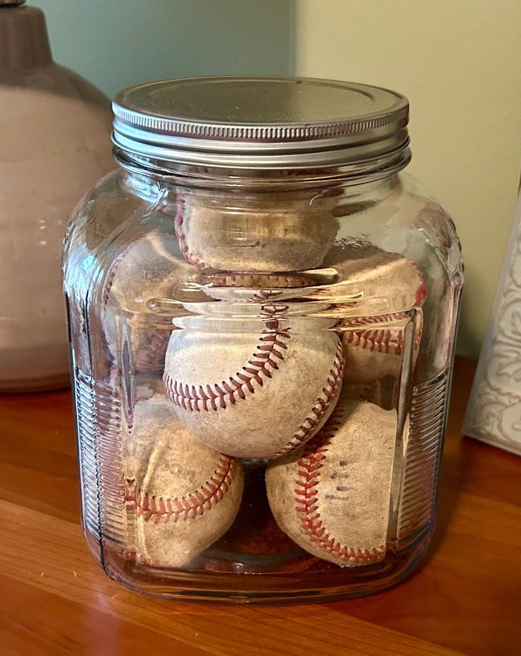 a glass jar filled with baseballs on top of a wooden table