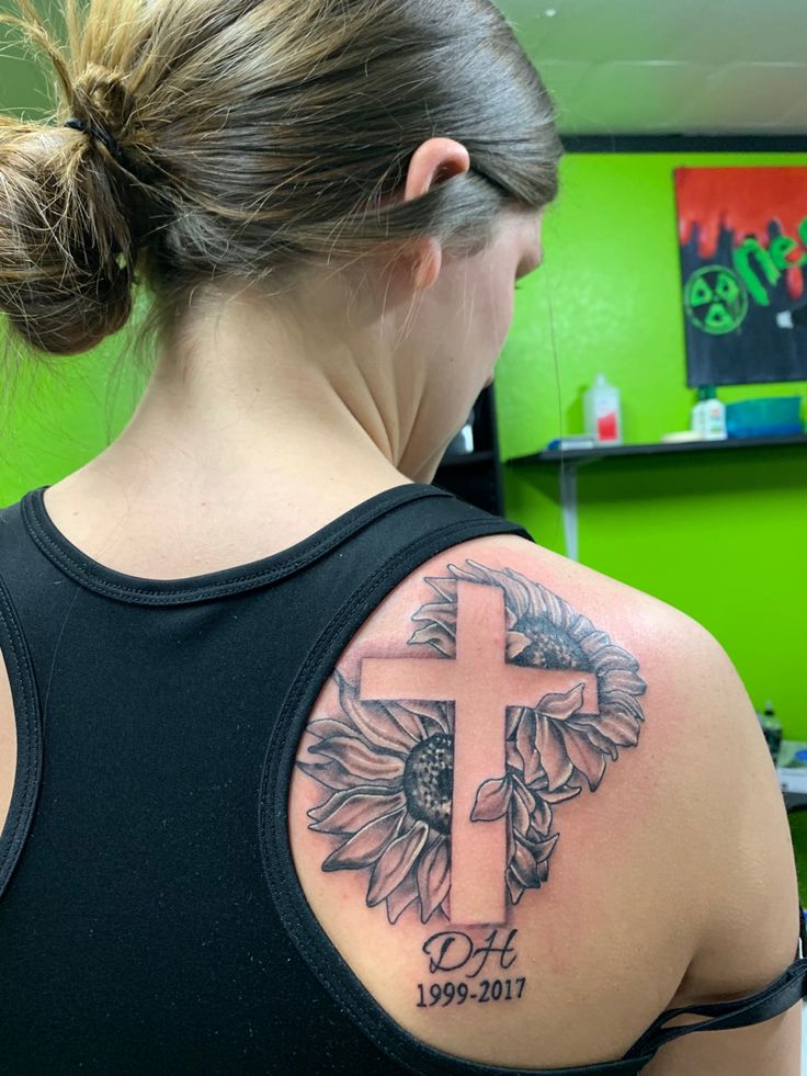 a woman with a cross and sunflowers tattoo on her back, behind her is a green wall