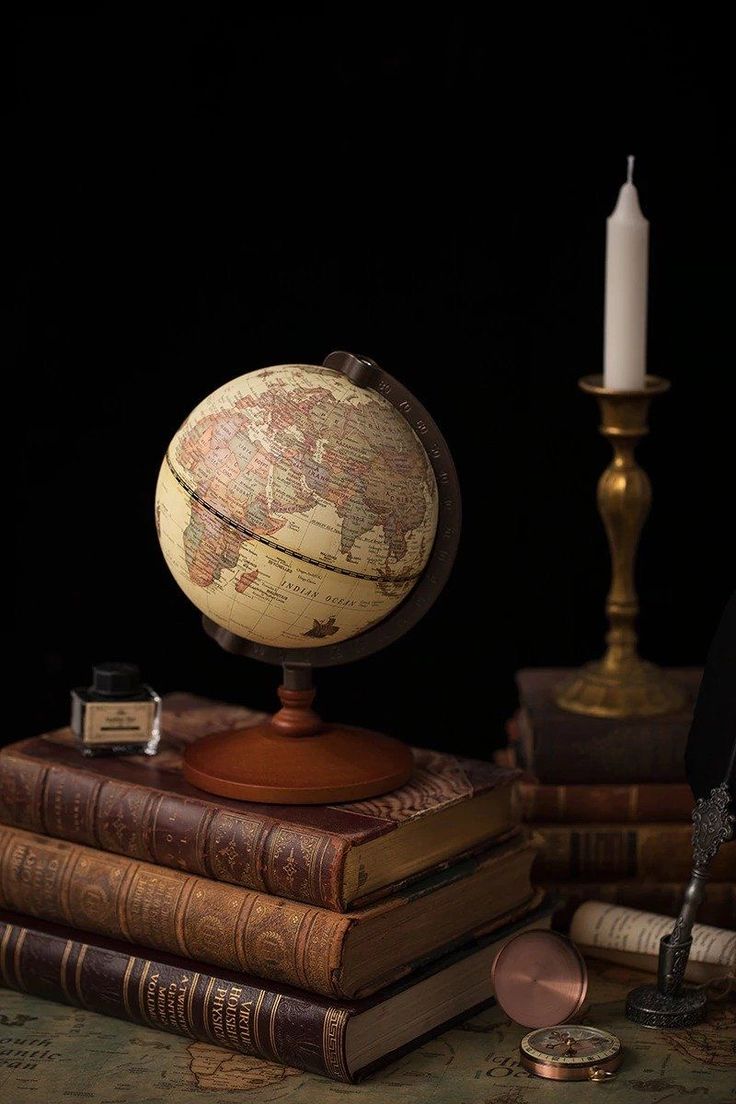 an old globe sitting on top of books next to a candle and some other items