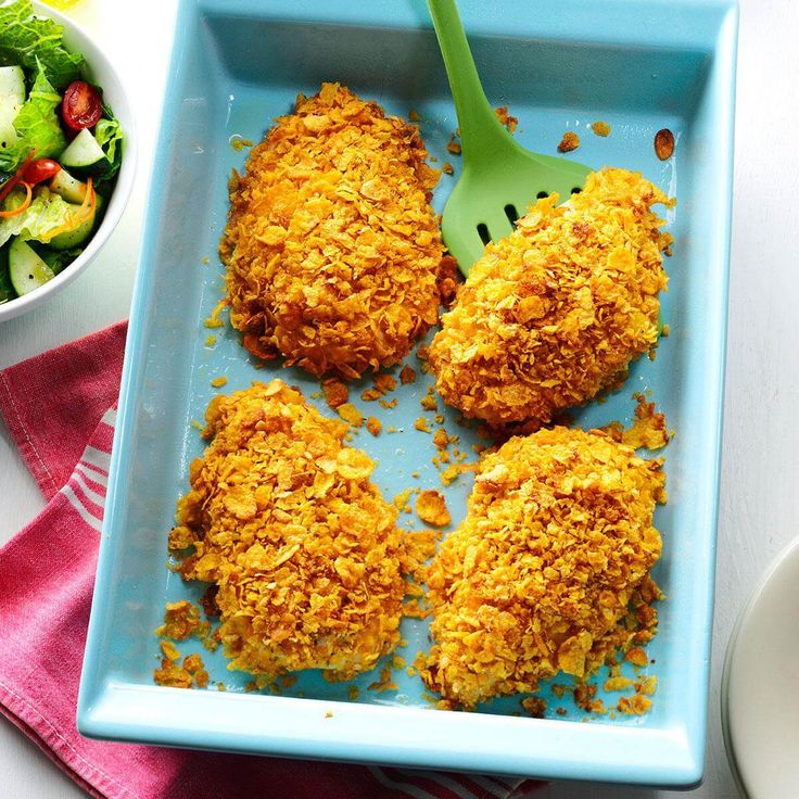 three fried chicken patties on a blue plate with a salad in the bowl next to it