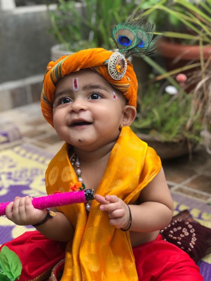 a small child wearing an orange outfit and holding a pink stick with a peacock feather on it