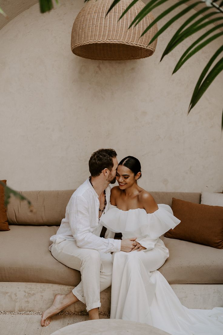 a man and woman sitting on a couch next to each other in front of a plant