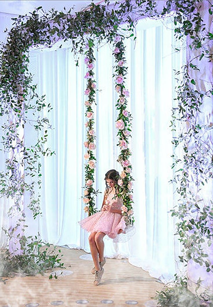 a woman in a pink dress is sitting on a swing with flowers and greenery