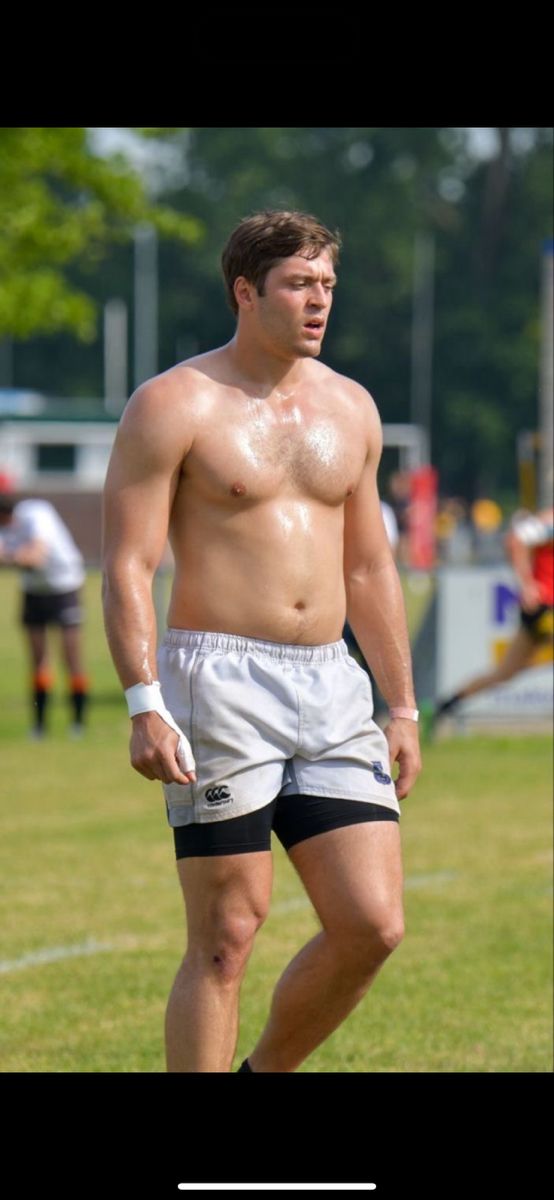 a shirtless man standing on top of a field holding a white frisbee