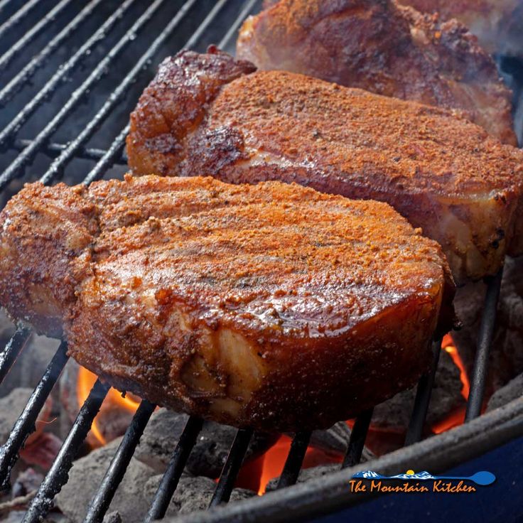 three steaks cooking on the grill with flames