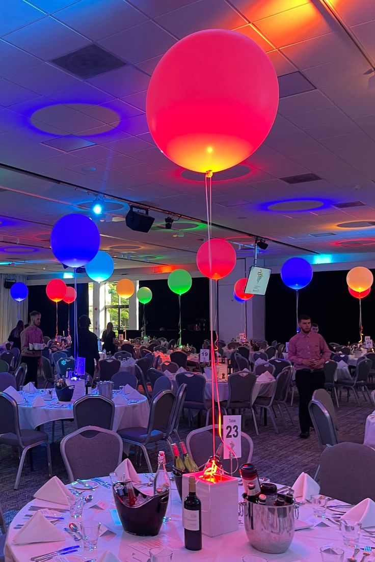 a room filled with lots of tables covered in white tablecloths and colorful balloons