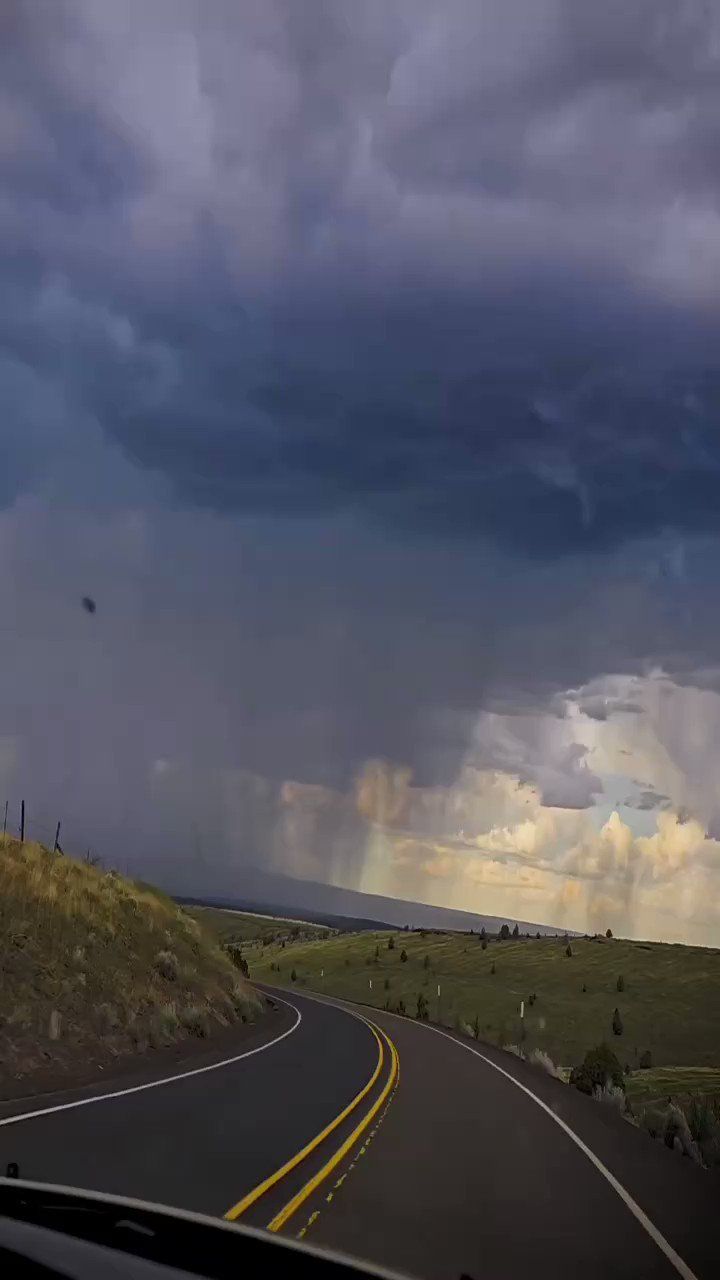 an image of storm clouds coming in from the sky over a road that has yellow and white lines on it