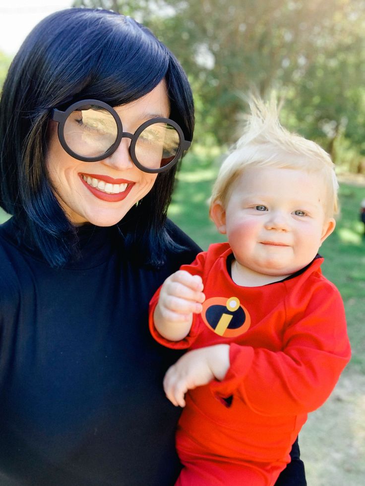 a woman holding a baby in her arms and smiling at the camera while wearing glasses