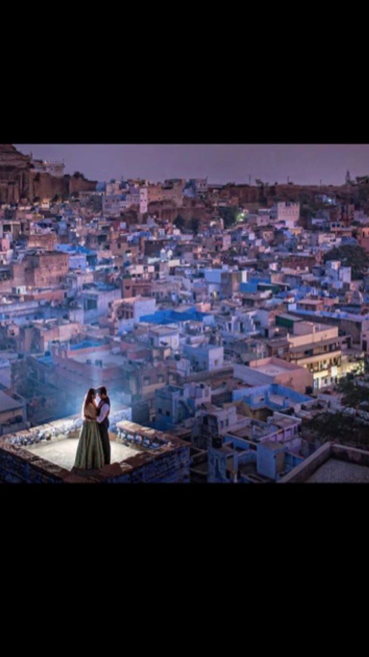 a man and woman standing on top of a roof in front of a cityscape