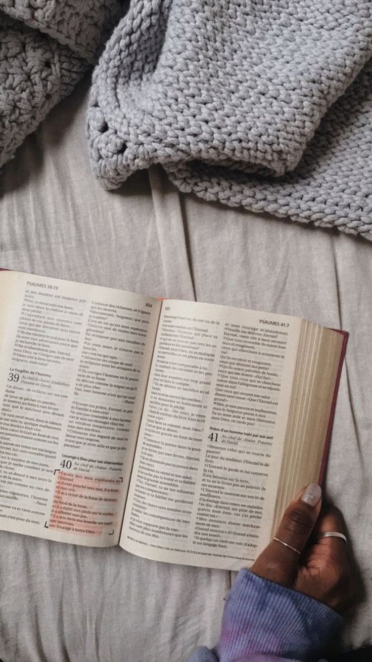 an open book laying on top of a bed next to two blankets and a blanket