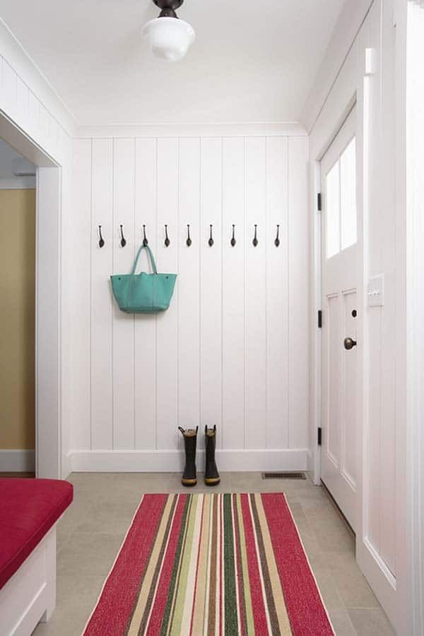 a hallway with white walls, striped rug and black boots on the floor next to a red bench