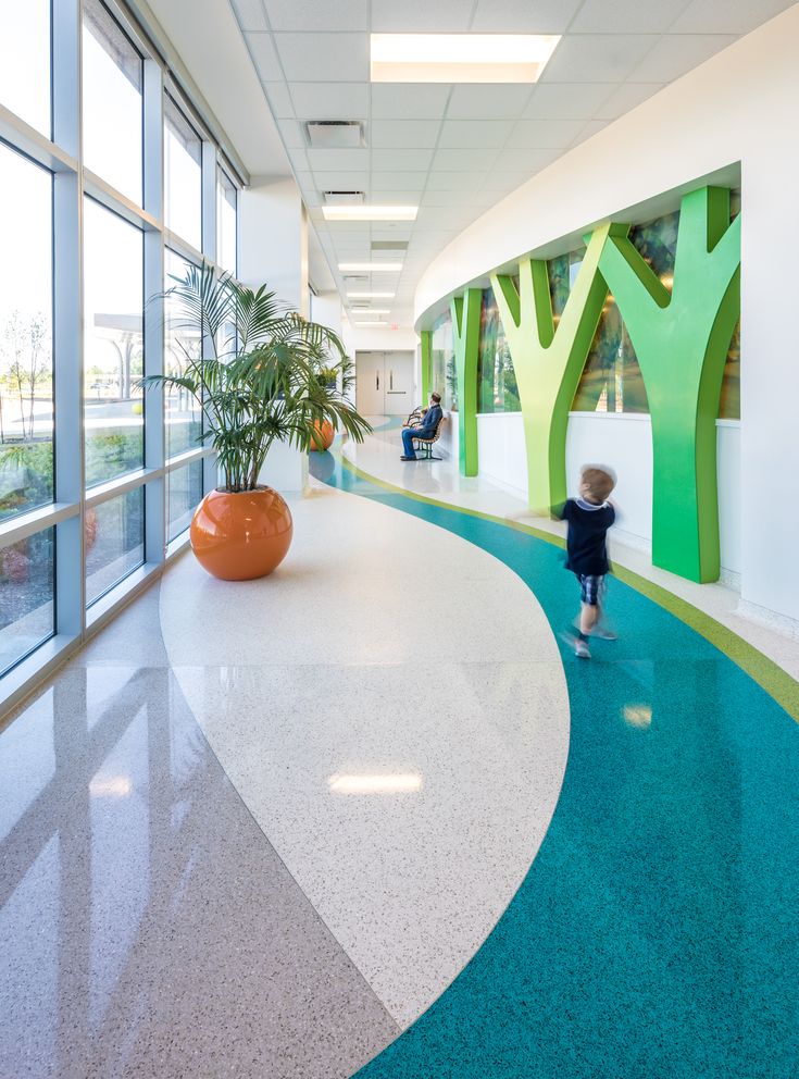 a little boy standing in the middle of an empty hallway with trees painted on the walls