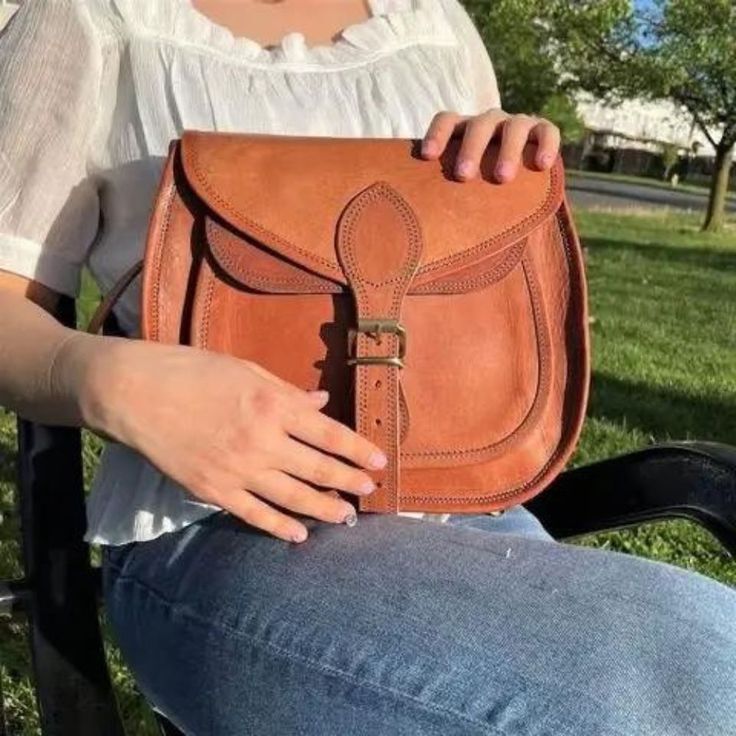 Rustic Goat Leather Crossbody Satchel Bag on model's lap Natural Color Satchel Shoulder Bag For On-the-go, Rectangular Satchel With Leather Strap For On-the-go, Everyday Use Saddle Satchel, Leather Handle Saddle Satchel, Daily Use Saddle Bag With Adjustable Strap, Brown Leather Strap Crossbody Bag, Everyday Saddle Flap Bag With Adjustable Strap, Saddle Satchel With Detachable Strap, Everyday Saddle Satchel With Detachable Strap