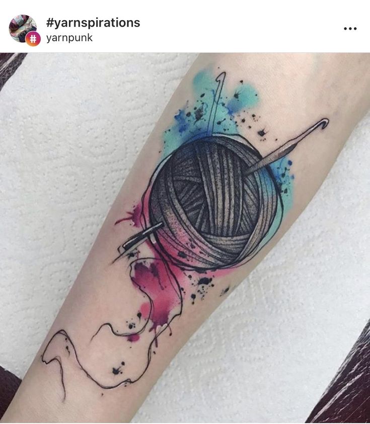 a person with a tattoo on their arm holding a ball of yarn and knitting needles