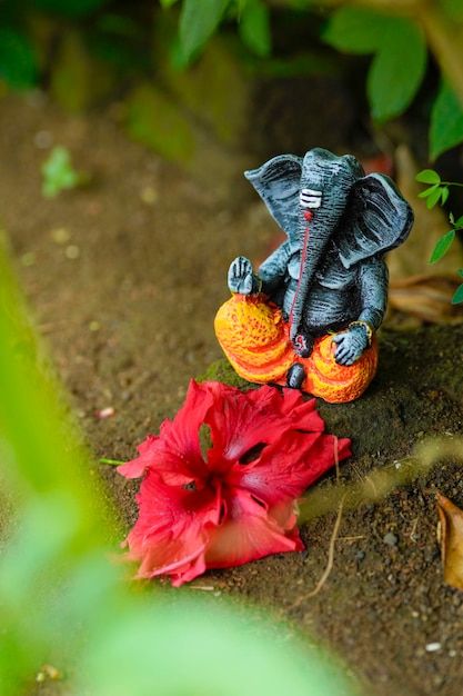 an elephant figurine sitting on top of a flower next to a red flower