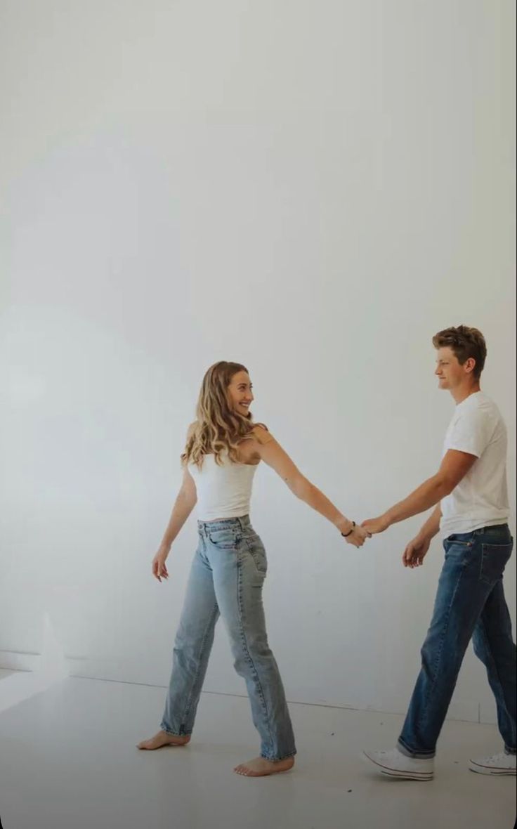 two people holding hands and walking in an empty room with one person looking at the camera