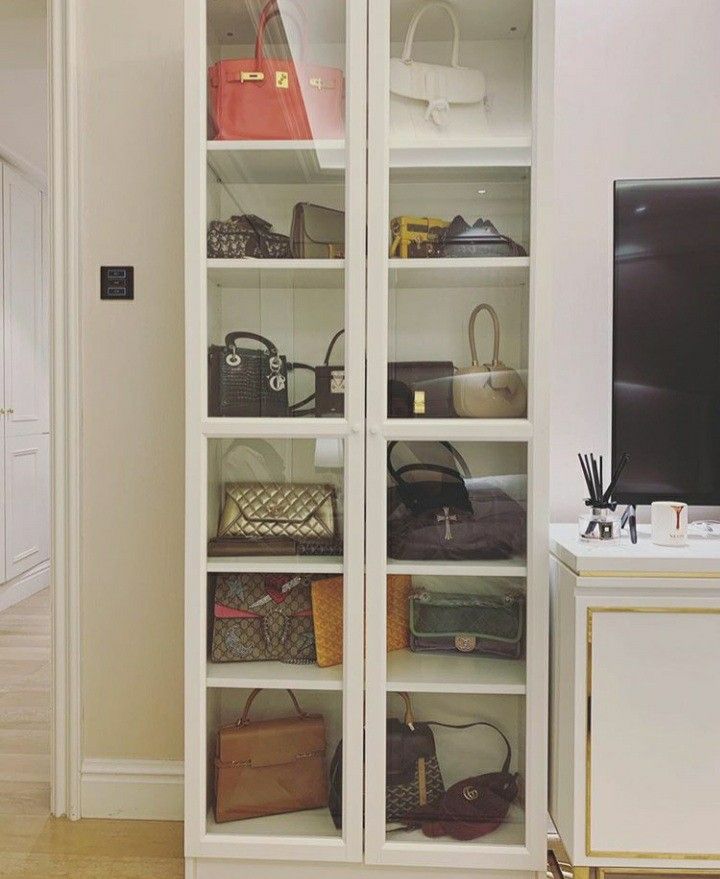 a white bookcase filled with lots of purses next to a tv on top of a dresser