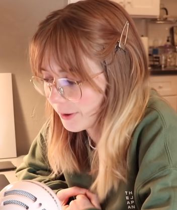 a woman with glasses is looking at a fan in her hand while sitting on the kitchen counter