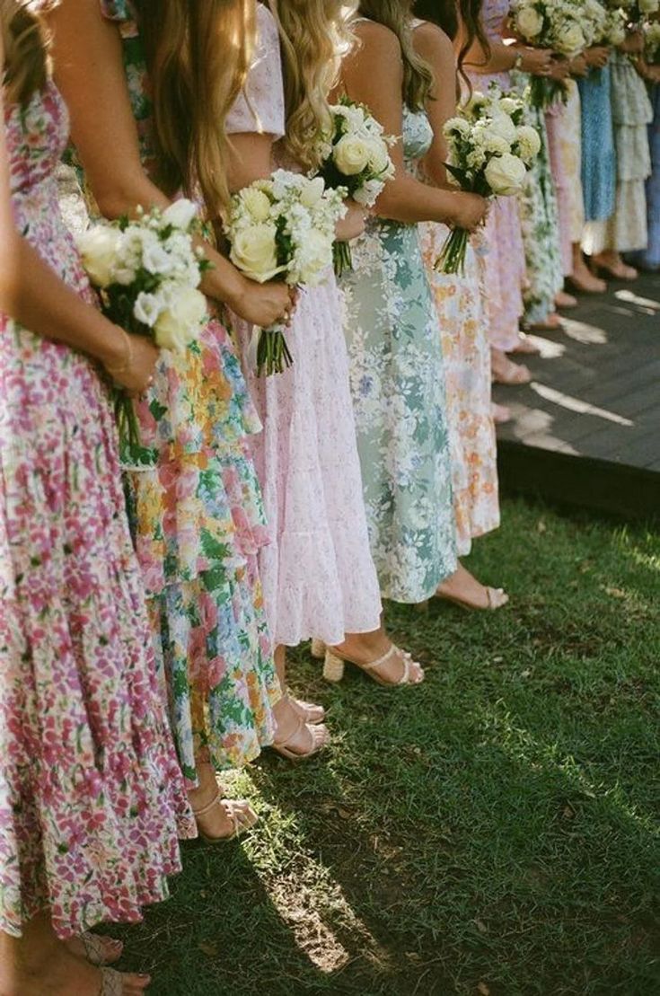 a group of women standing next to each other holding bouquets in their hands and wearing dresses with flowers on them