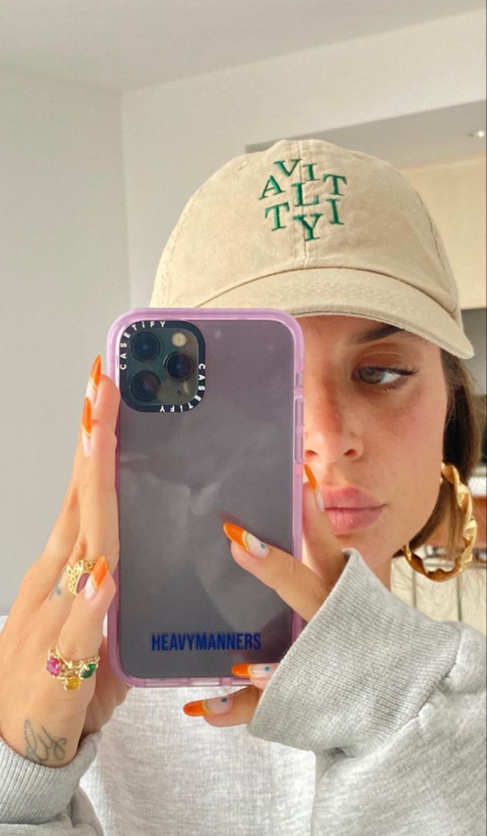 a woman wearing a hat and holding up her phone to take a selfie in the mirror