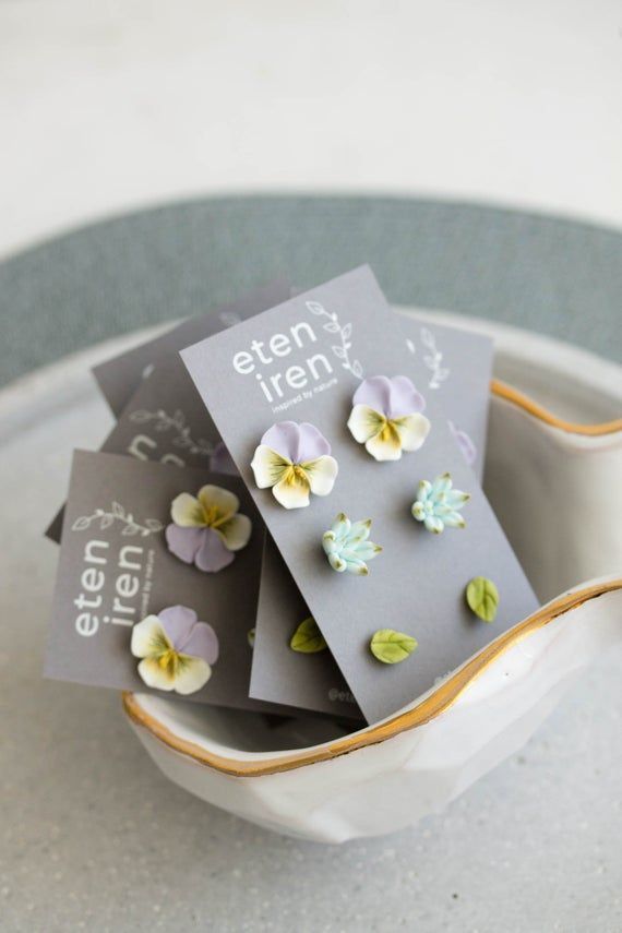 three small flower earrings in a white bowl on top of a table with an empty card