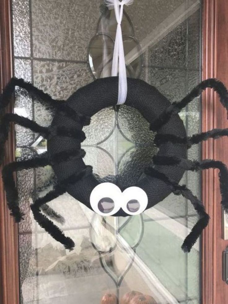 a spider made out of yarn sitting on top of a glass door with googly eyes