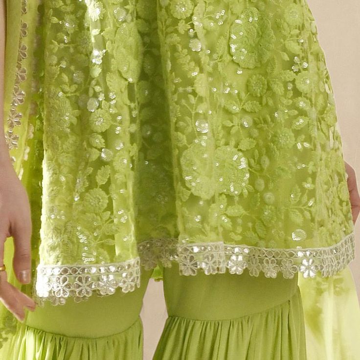 This exquisite Lime Green Embroidered Kurta Sharara Set exudes elegance and tradition. Crafted from soft net fabric, the strappy lime green kurta is adorned with intricate floral embroidery, shimmering silver sequins, and delicate thread work, with a hemline beautifully finished with cutwork gota lace for a refined touch. Teamed with a voluminous, flouncy sharara is gathered from the thigh, featuring a striking gota and mirror-embroidered hem that radiates glamour. A matching tulle dupatta grace Strappy Kurta, Georgette Kurta, Kurta Sharara Set, Kurta Sharara, Embroidered Hem, Indian Wedding Wear, Sharara Set, Net Fabric, Net Dupatta