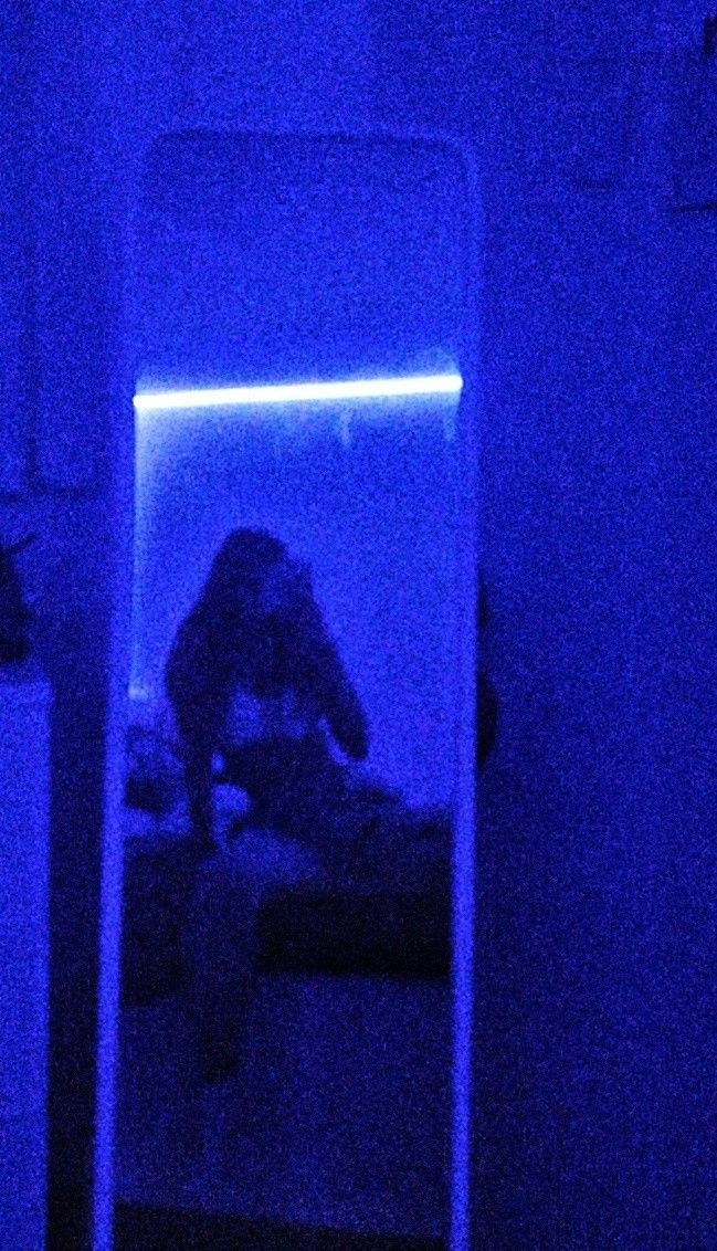 a person sitting on a bed in a room with blue light coming through the mirror