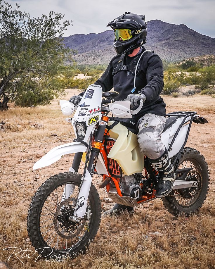 a man riding on the back of a dirt bike in an open field with mountains in the background