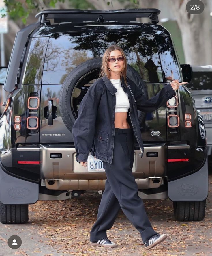 a woman standing in front of a black suv with her hands out to the side