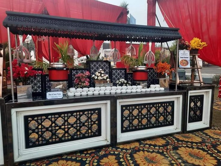 a buffet table with flowers and candles on it in front of a red curtained area