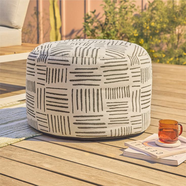 a white and black ottoman sitting on top of a wooden deck next to a cup