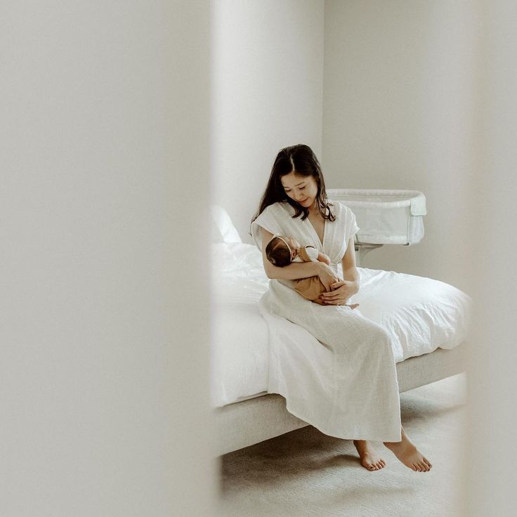 a woman holding a baby in her arms while sitting on a white bed with pillows