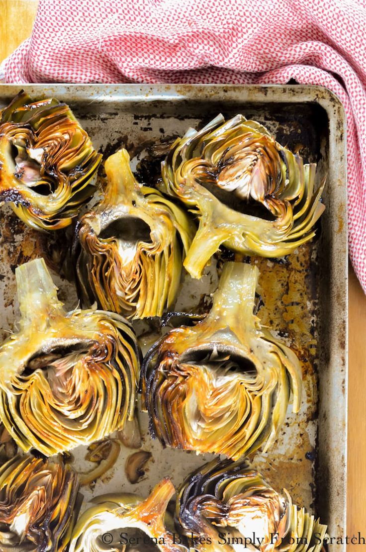 roasted artichokes in a baking pan with a red towel on the side