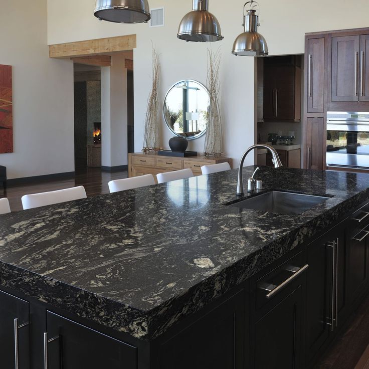 a large kitchen with marble counter tops and black cabinets, along with an island in the middle