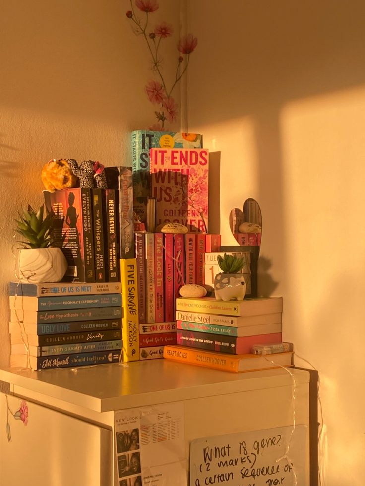 a refrigerator covered in lots of books next to a wall with flowers and plants on it