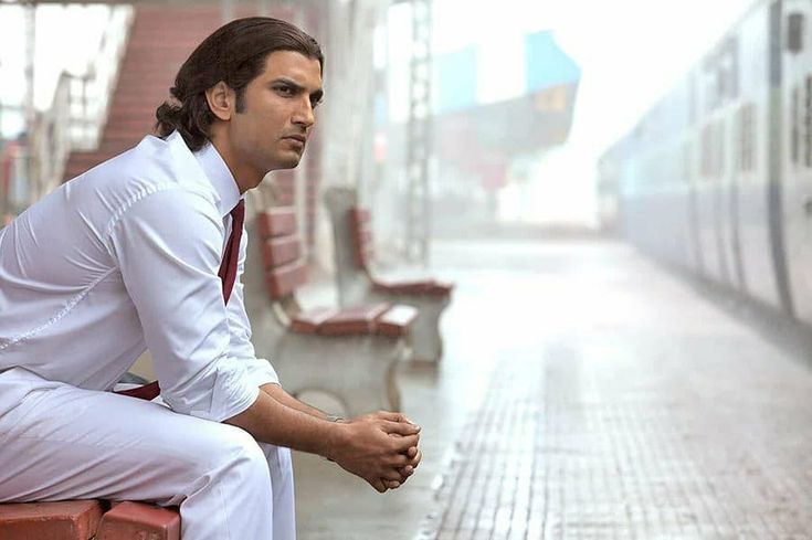 a man in white shirt and red tie sitting on bench next to train tracks,