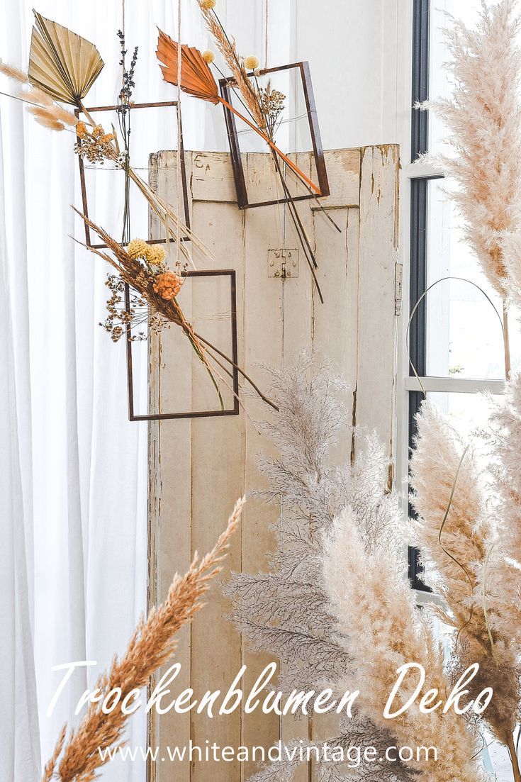 dried flowers are hanging on the wall in front of an open window with white curtains