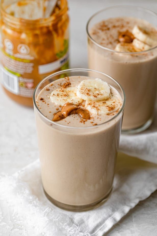 two glasses filled with food sitting on top of a white cloth next to a jar of peanut butter