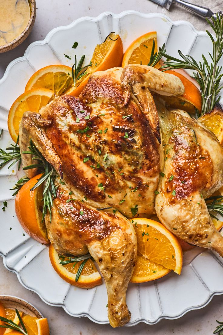 a whole chicken on a platter with oranges and rosemary garnishes