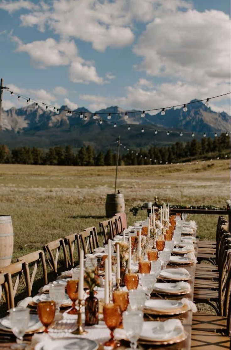 a long table is set with plates and wine glasses for an outdoor dinner in the mountains