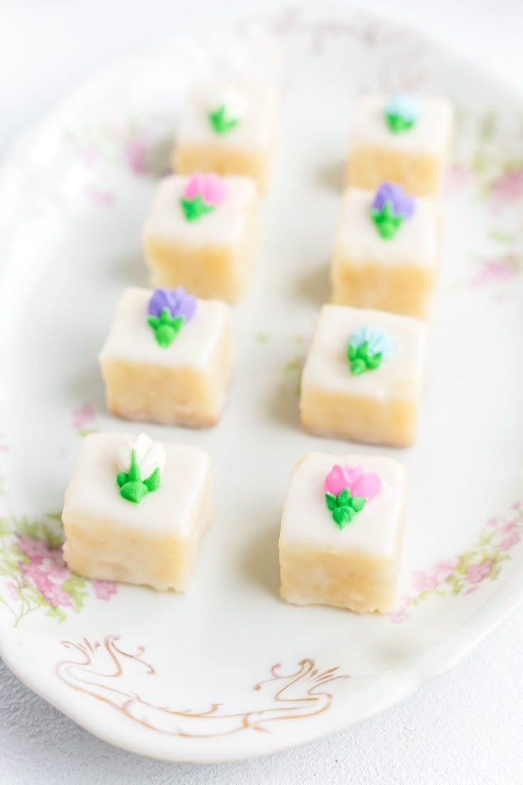 small pieces of cake sitting on top of a white plate with flowers and leaves painted on it