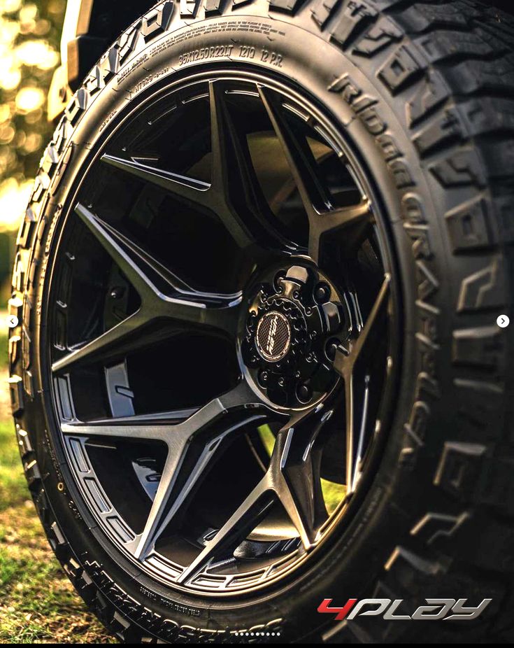 the front wheel and tire of a car on some grass with trees in the background